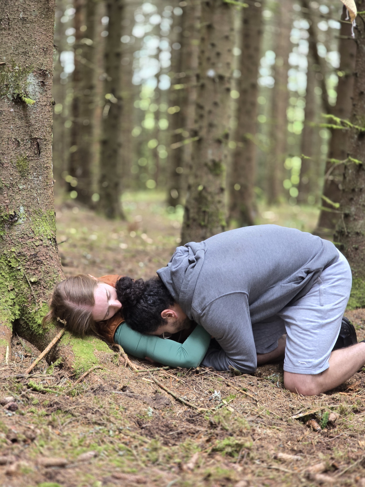 Two performers physically entangled at the roots of a tree