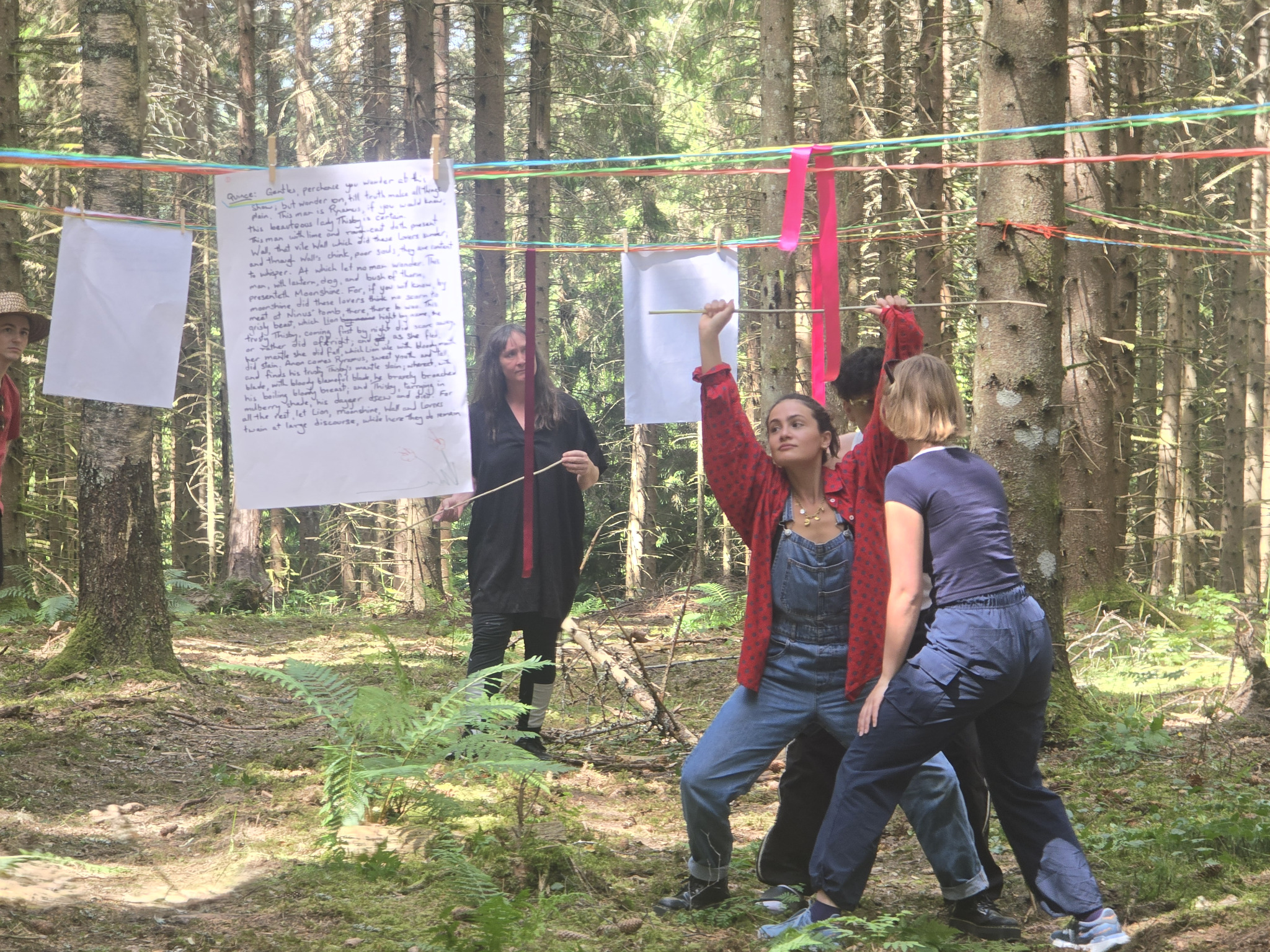 Performers moving among handwritten Shakespeare text suspended between trees