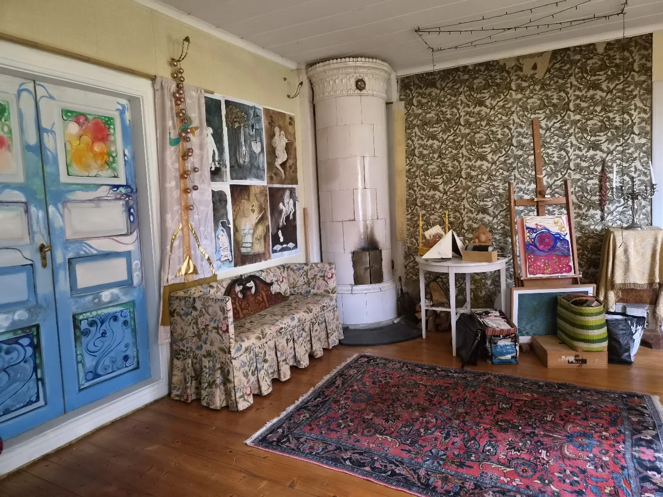 Room filled with paintings, a painted blue door and a traditional Swedish tiled stove