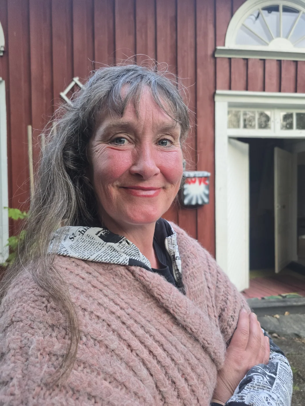 Portrait of artist Rina Beldo outside a red building at Norra Backen